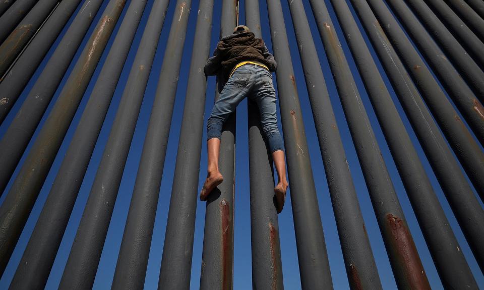  Someone from the migrant caravan tries to clamber over the tall barrier