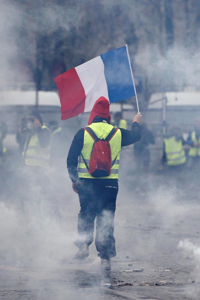  A protester wearing a yellow vest, a symbol of a French drivers' protest against higher diesel taxes, holds a French flag