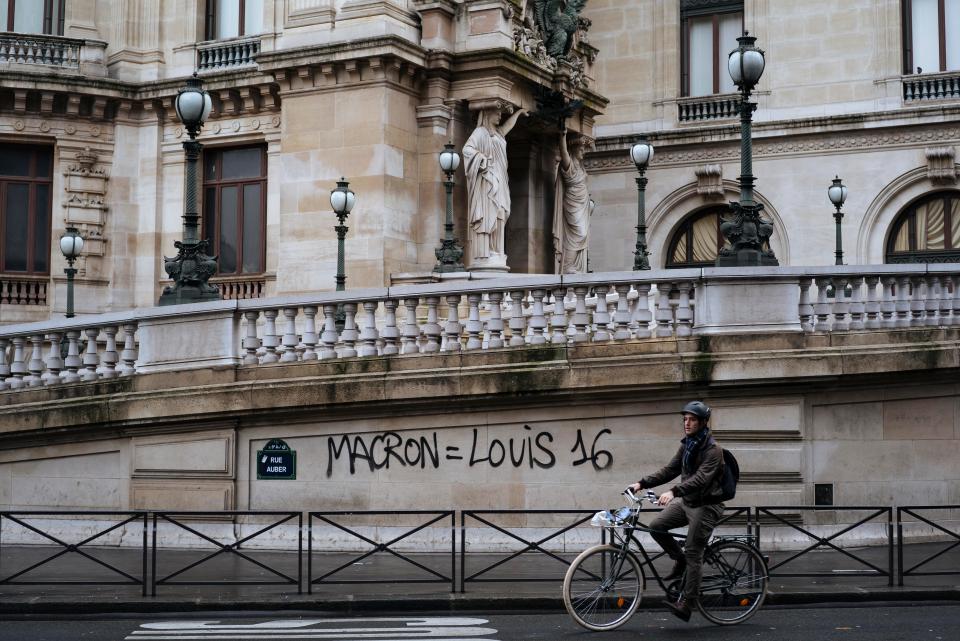  A cyclist rides by graffiti that says 'Macron equal to Louis 16'