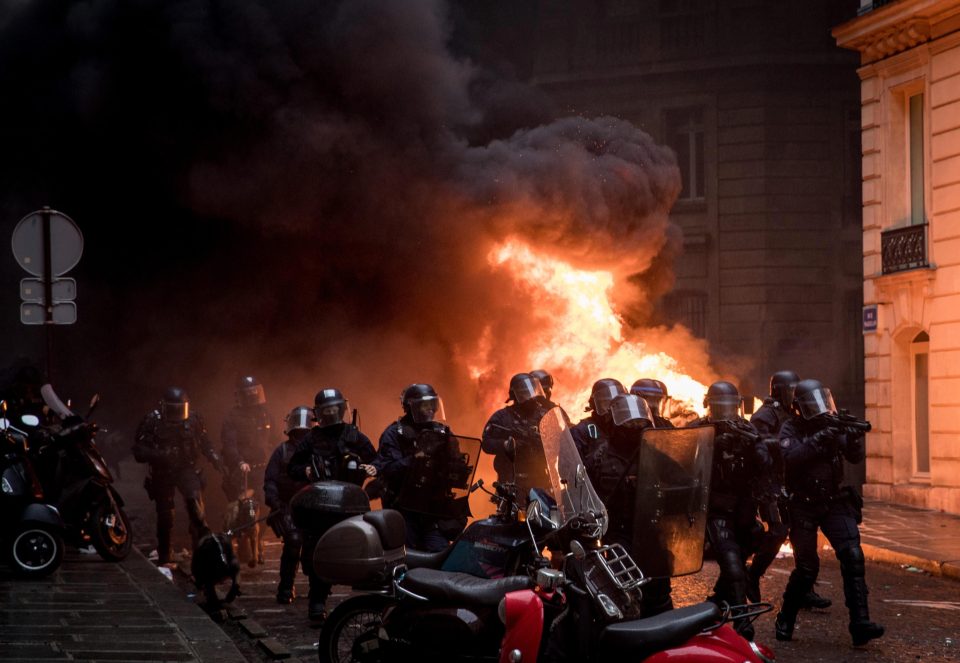 Police run past a burning car as they push protesters back during a 'yellow vests' demonstration near the Arc de Triomphe