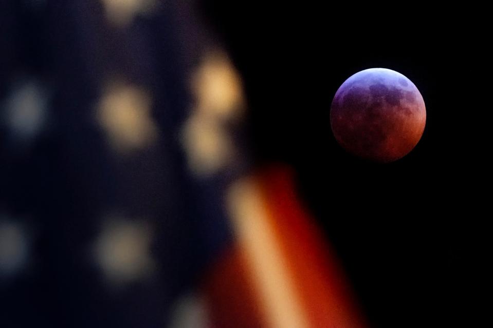  The moon creeps out from behind an American Flag waving in Washington DC