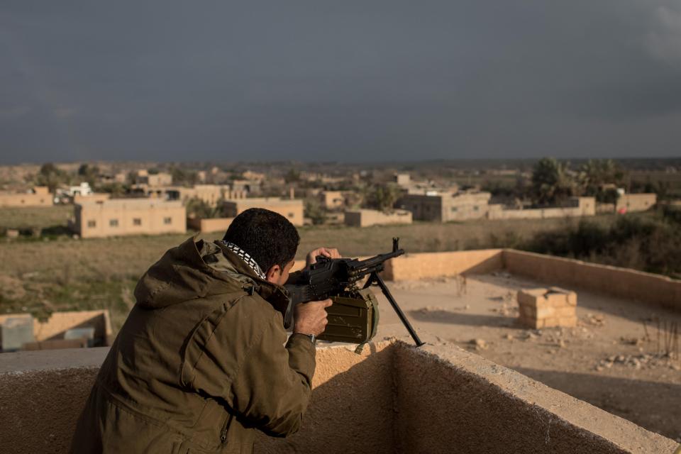 An SDF soldier takes up position on a roof top ready to mow down ISIS troops should they flee their under fire positions