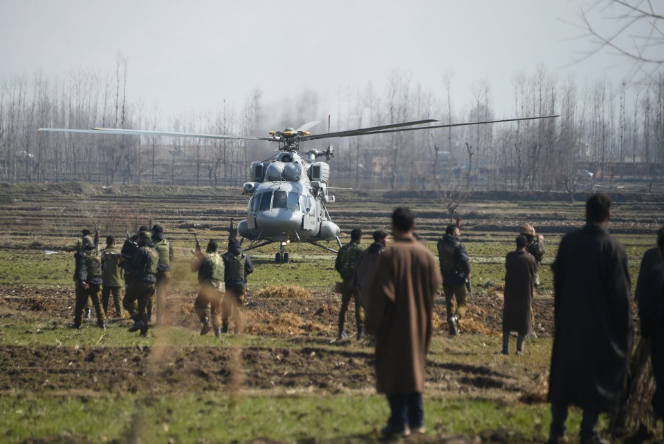 Indian soldiers and Kashmiri onlookers stand near an Indian army helicopter that landed near the site where an Indian aircraft crashed