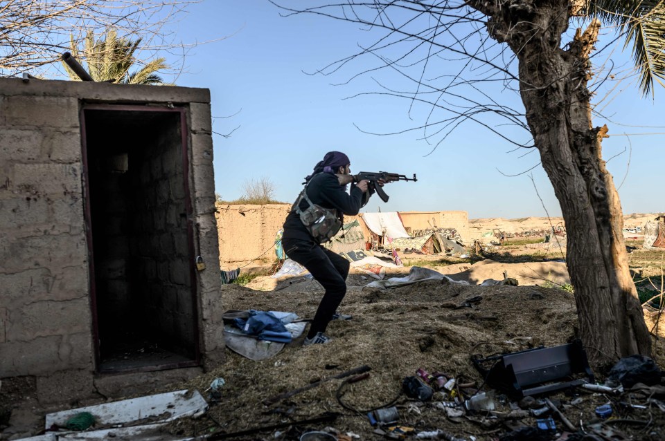 A fighter with the Syrian Democratic Forces (SDF) takes aim with his Kalashnikov assault rifle after seeing a man walking towards his position in the town of Baghouz