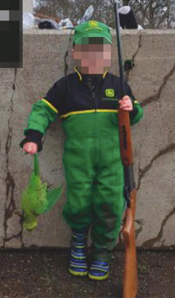 A smiling lad, 4, poses with a single-barrel .410 and a dead parakeet he has just shot