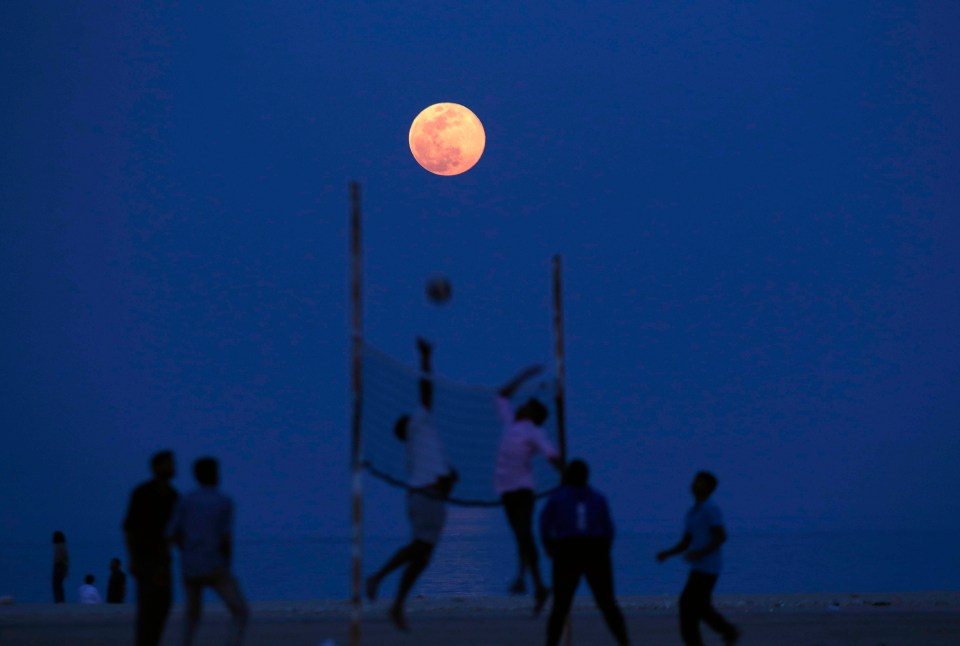 Friends playing volleyball beneath the pink moon near Kuwait City