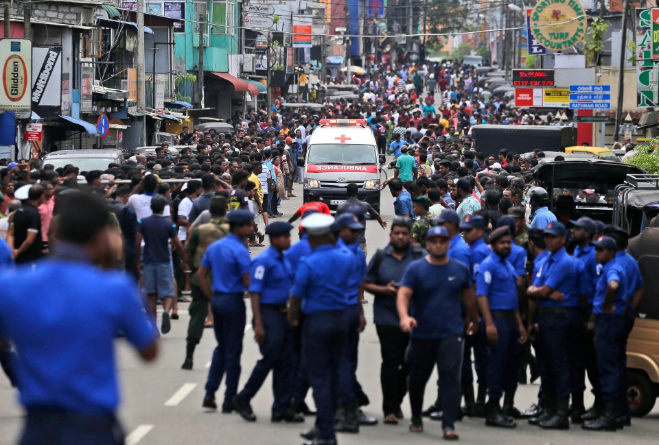 Police officers clear a road in Colombo as an ambulance drives through