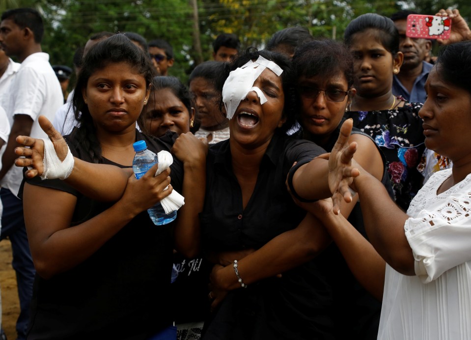 A grieving woman who lost her husband and two children in the depraved church bombing cries towards their graves in Negombo