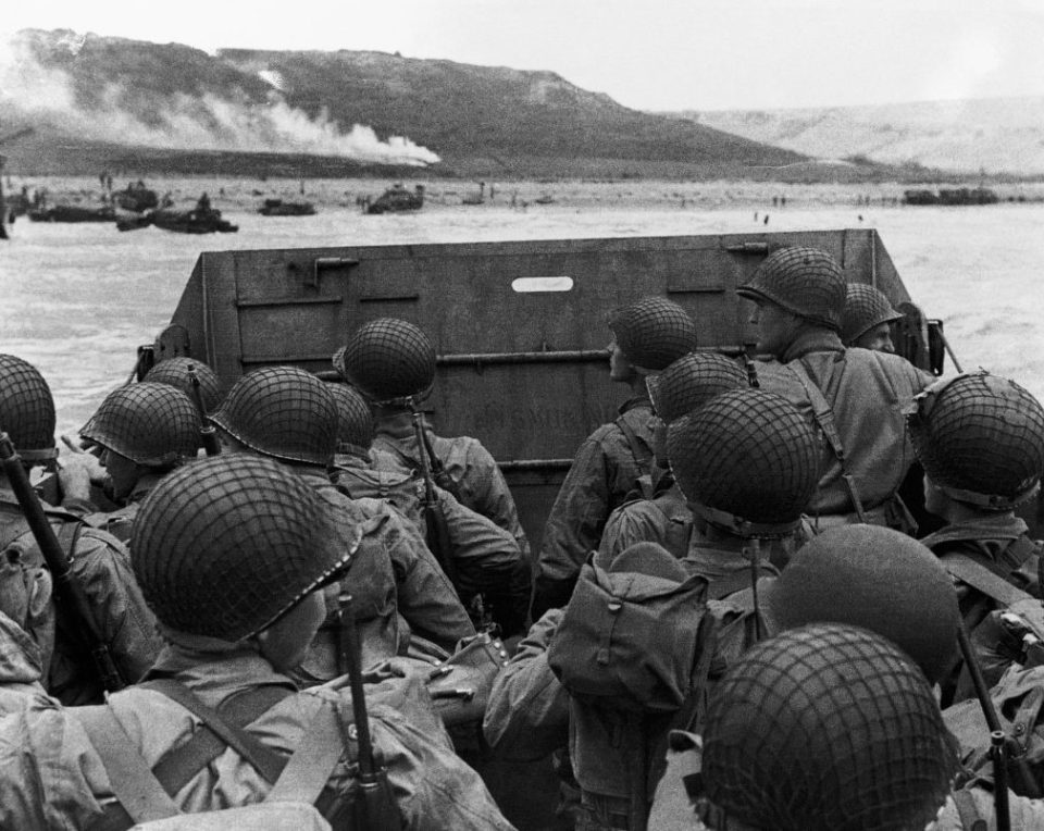  Men of a follow-up wave landing observe the Omaha coastline with the bluffs close to the seashore