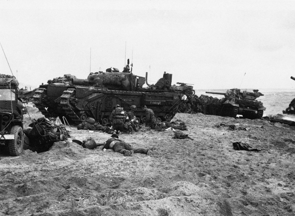  Soldiers hunch behind an AVRE taking cover from machine gun fire as in the background an M10 tank destroyer known in British service as a ‘Wolverine’ swings its turret to engage a bunker