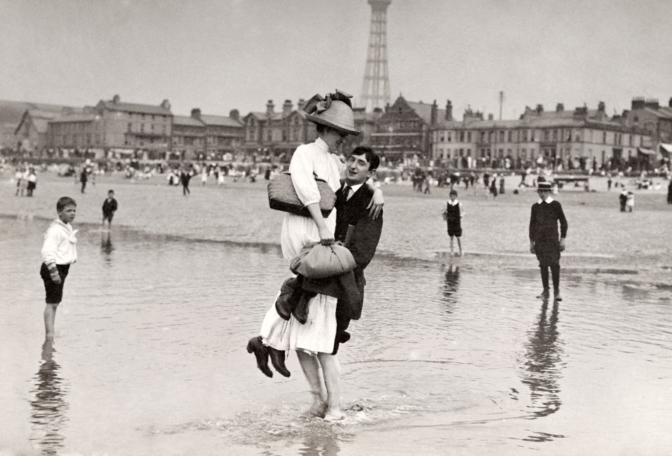  A young man holding a young woman whilst paddling in the sea at Blackpool, circa 1912