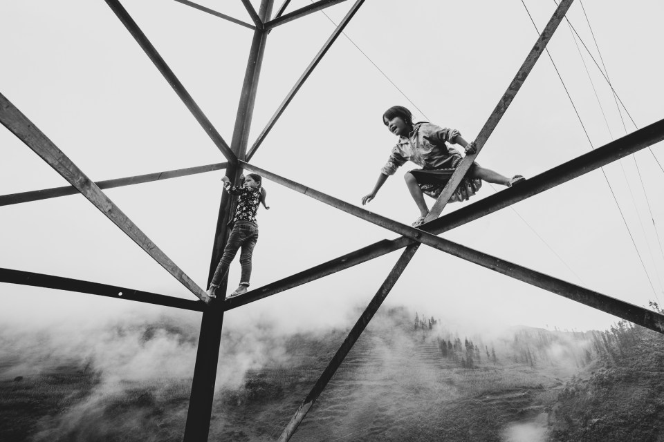  Two girls climb an electric pylon in the mountains in Bac Ha, Vietnam