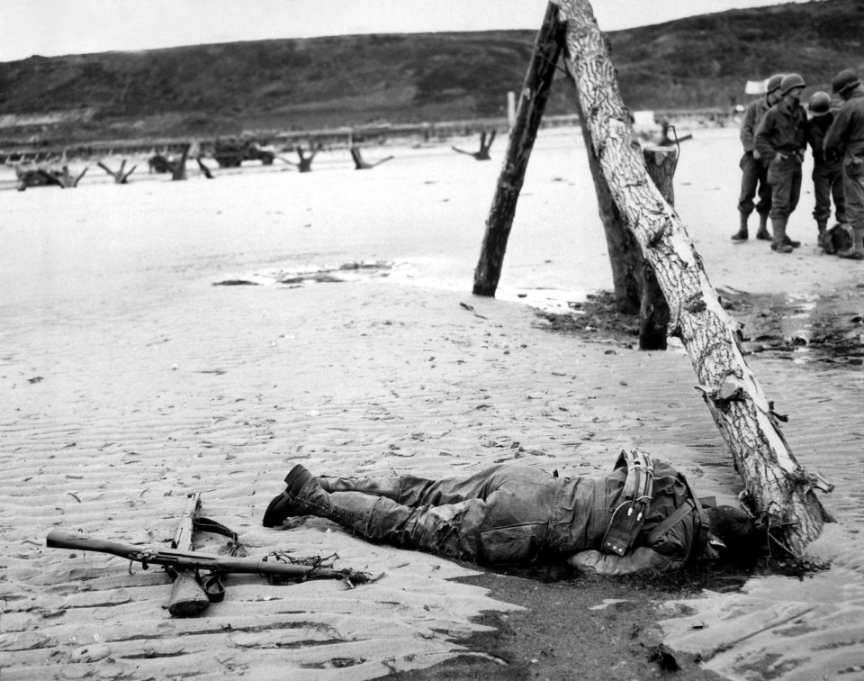  Crossed rifles in the sand are a comrade's tribute to this American soldier who sprang ashore from a landing barge and died at the barricades