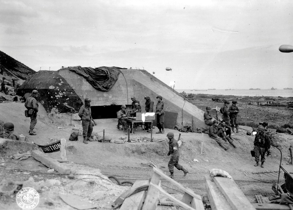  US Army troops congregate around a signal post used by engineers on the site of a captured German bunker overlooking Omaha Beach after the D-Day landings