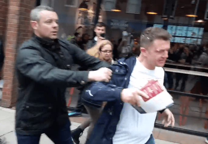  A supporter holds back an angry Tommy Robinson after he is pelted with milkshake in Bury