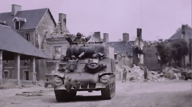  A US army tank rolls into a town destroyed by bombing from the war