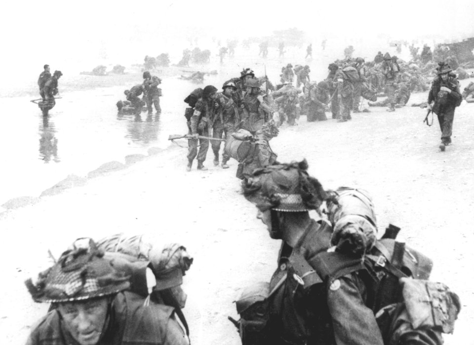  British soldiers, many injured, land on Sword Beach. In the foreground are Royal Engineers sappers, behind them heavily laden medical orderlies