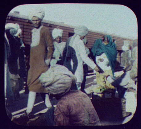  Crowds board a train while a vendor sells food on the platform