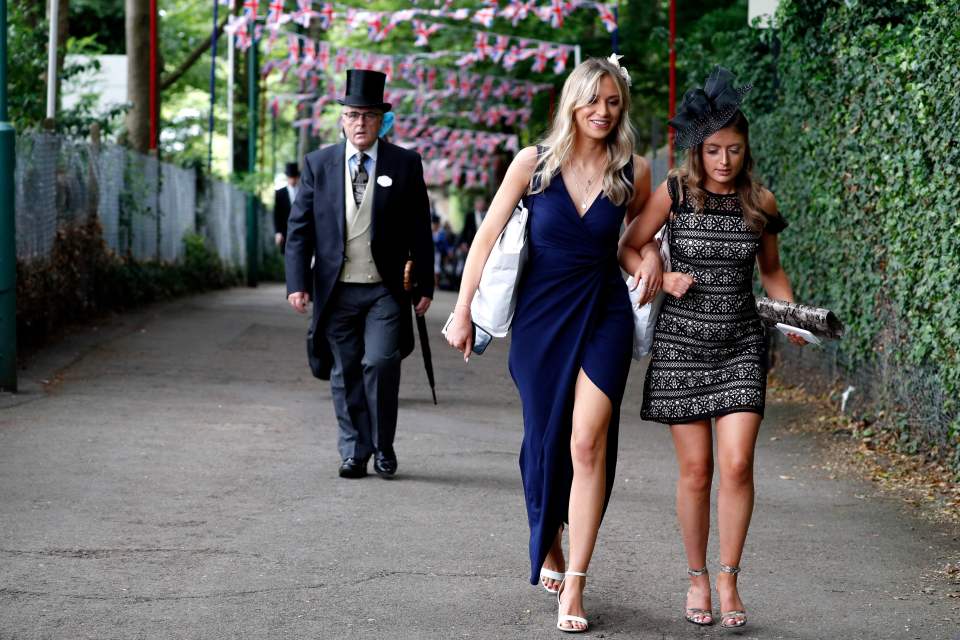 Two racegoers walk arm in arm as they head into Ascot