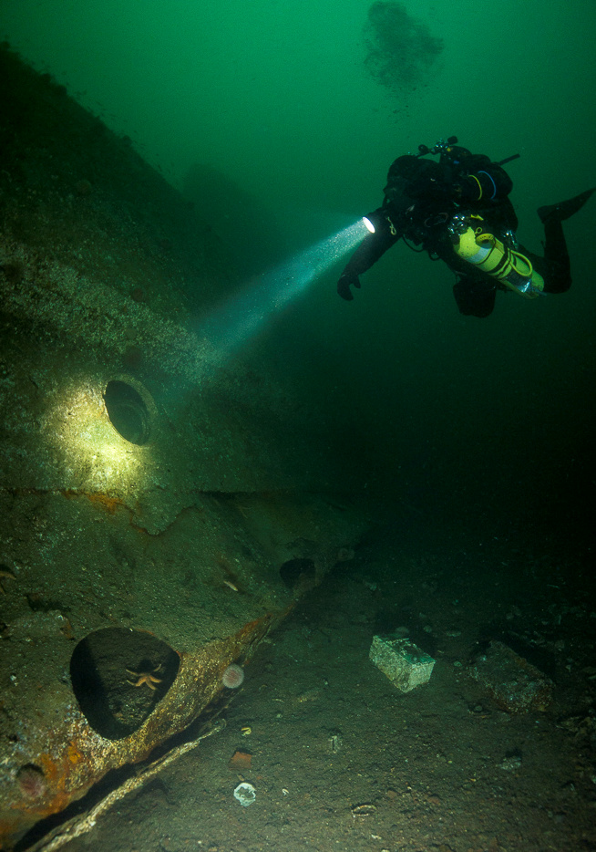 A diver swims by a porthole on the sunken SMS Markgraf