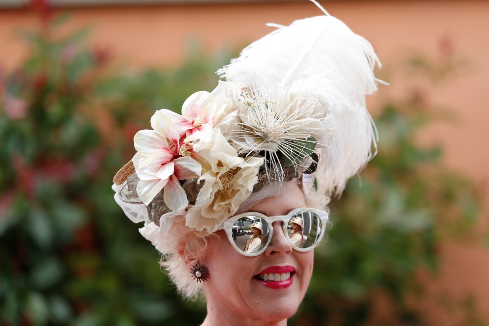 This woman wears bright lipstick and mirrored glasses as she has a floral and feathered fascinator on