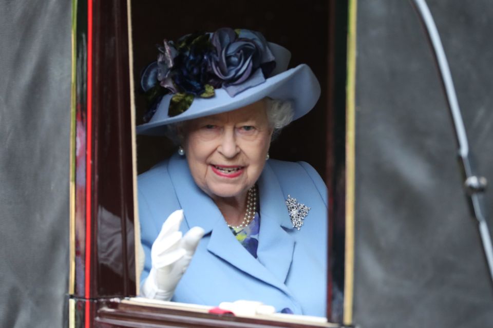 The Queen waves to crowds while wearing a pale blue