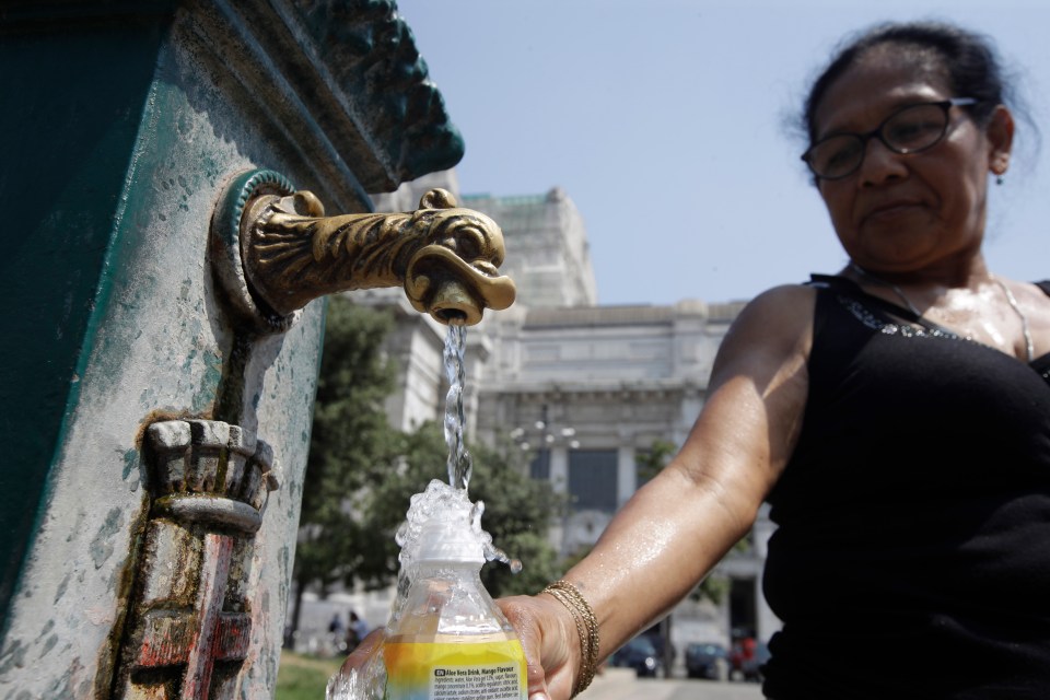  A woman fills a bottle of water from a fountain outside Milan's central railway station, Italy