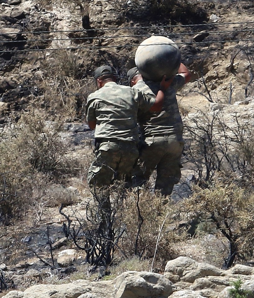  Military personnel carry debris on a slope where the missile struck