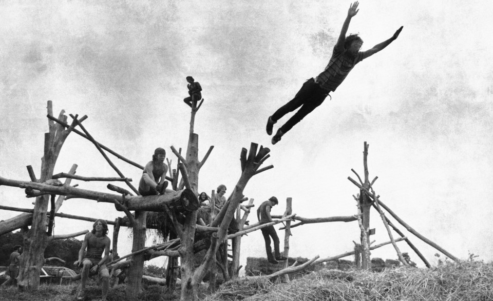  Music fans sit on a tree sculpture as one leaps mid-air onto a pile of hay during the Woodstock Music and Art Festival in Bethel, New York