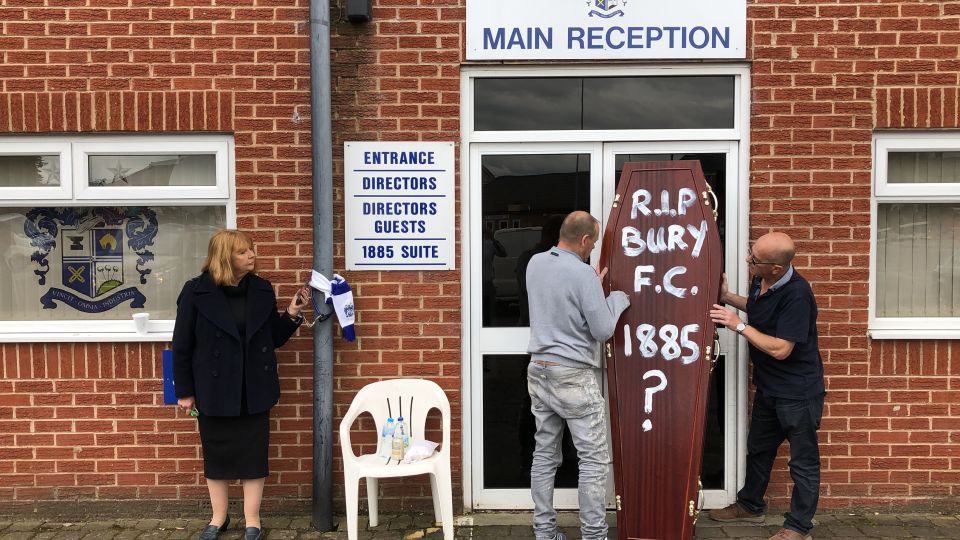  Two Bury fans arrived with a coffin and placed it outside the entrance to Gigg Lane as former director Joy Hart chained herself to drainpipe in protest