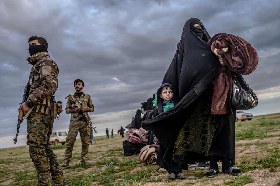  Kurdish forces stand guard as a woman with her child walks past after she has left Baghouz