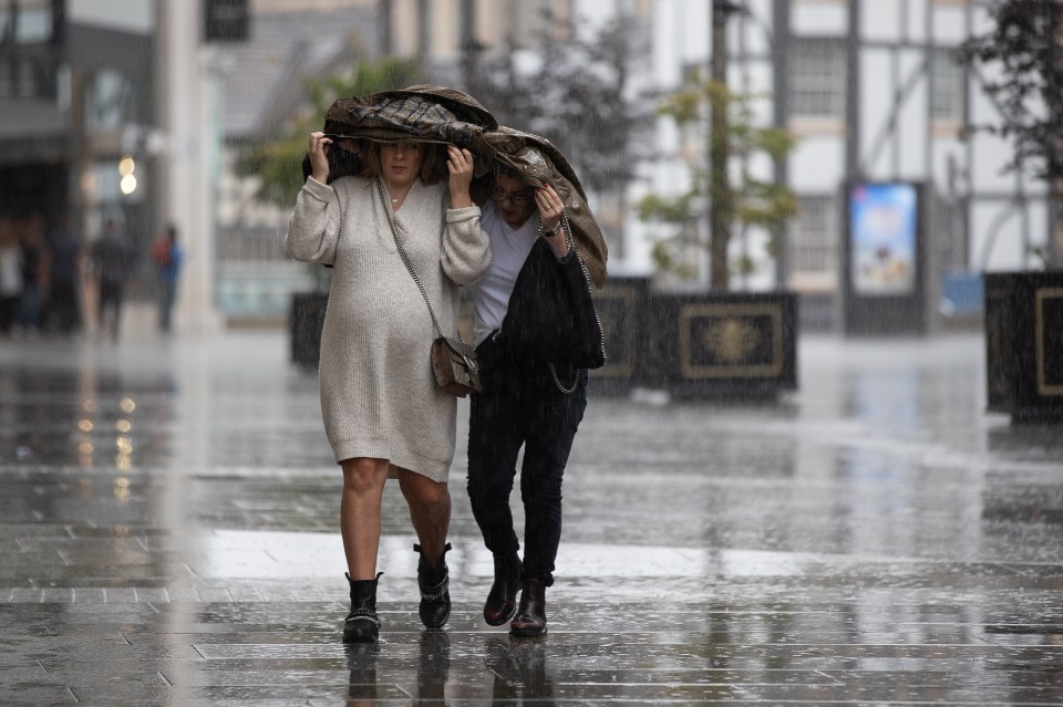  Two women on Cathedral Street use a jacket to shelter during a heavy downpour in Manchester City Centre on Saturday