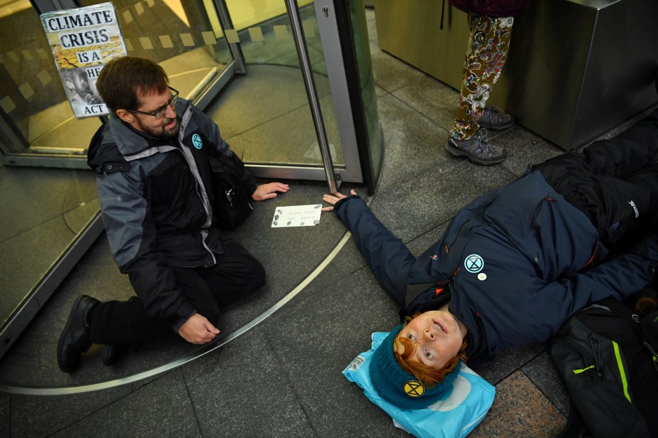 A protester lies on the ground after she glued herself to revolving door of Baclays Bank in Canary Wharf