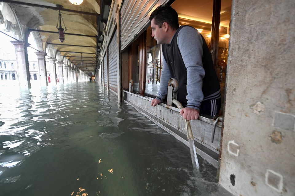  A man pumps water from a shop as high tide in the Lagoon reaches its peak