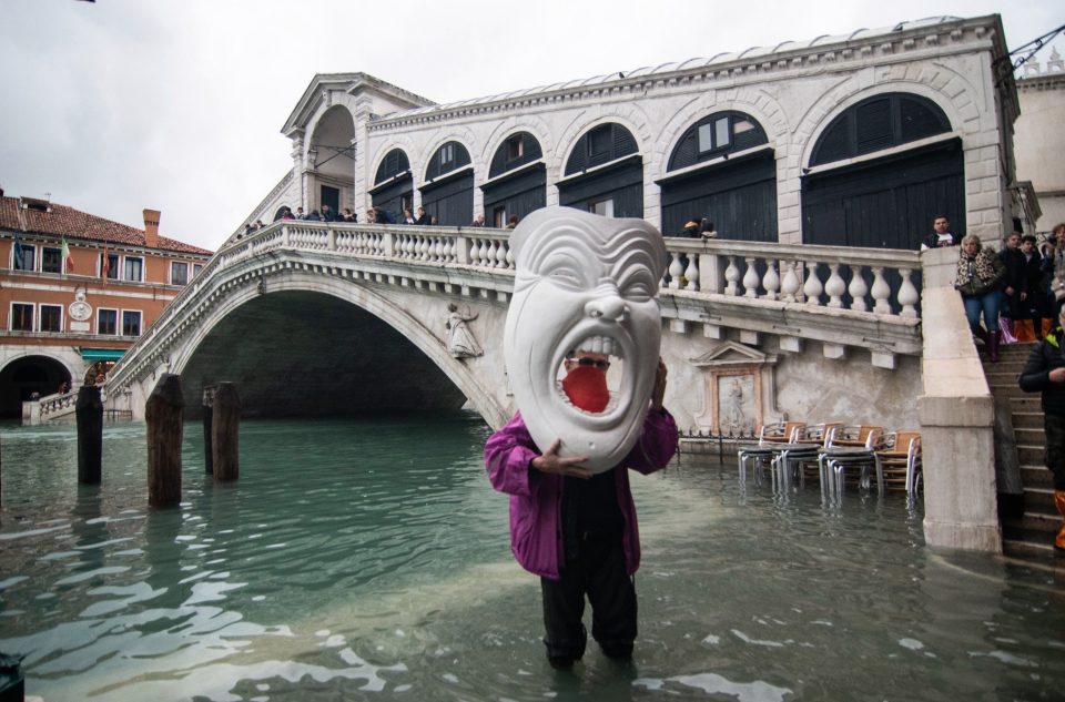  A man with a giant mask stands close to Rialto bridge during an exceptionally high tide on November 17