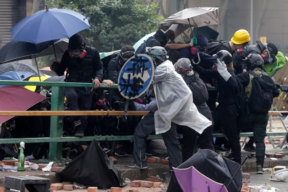 Protesters with umbrellas and gas masks retreat from the police