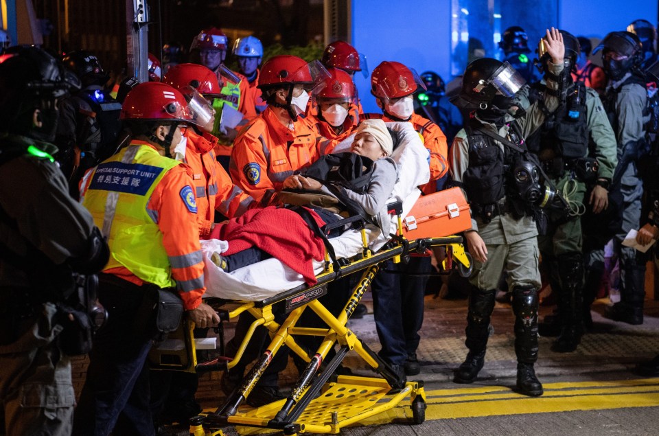 An injured protester is carried out on a stretcher bed by multiple rescue workers as police look on