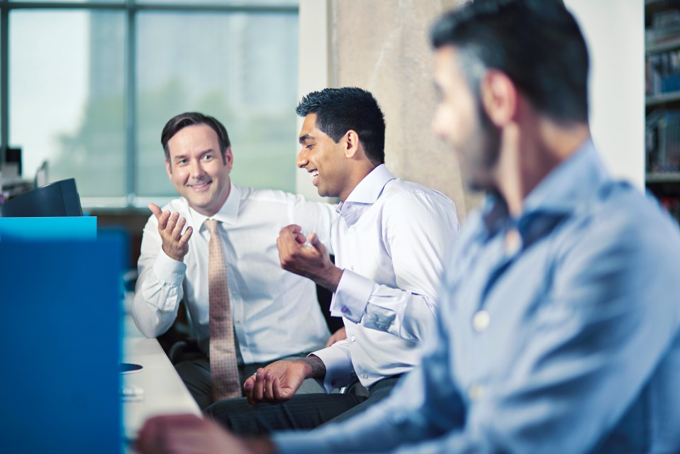 Three office workers talking at their desks.