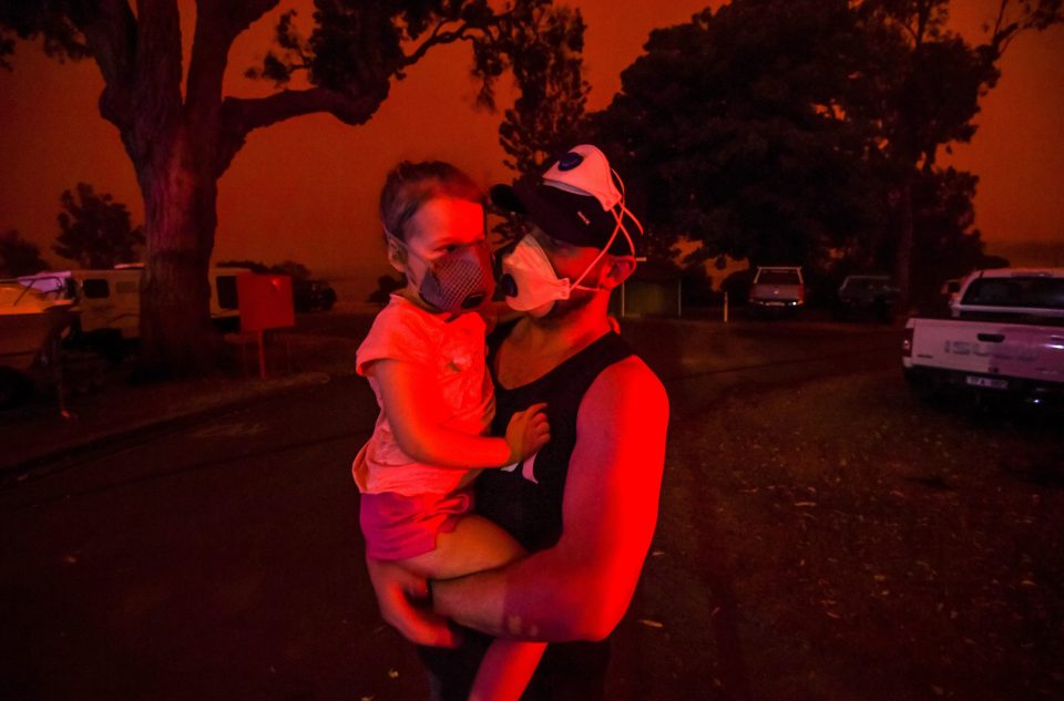  A resident holds his daughter as the skies above go red in the middle of the day amid raging fires