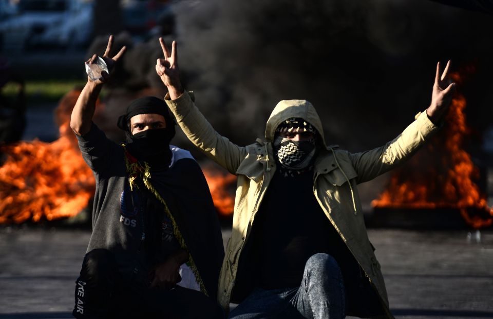  Iraqi demonstrators flash the victory sign next to burning tyres as angry protesters blocked roads in the central shrine city of Najaf