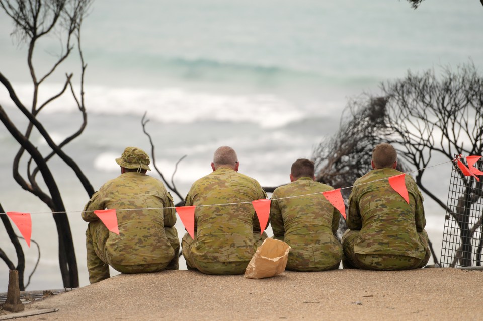  Soldiers sit on a beach amongst burnt trees