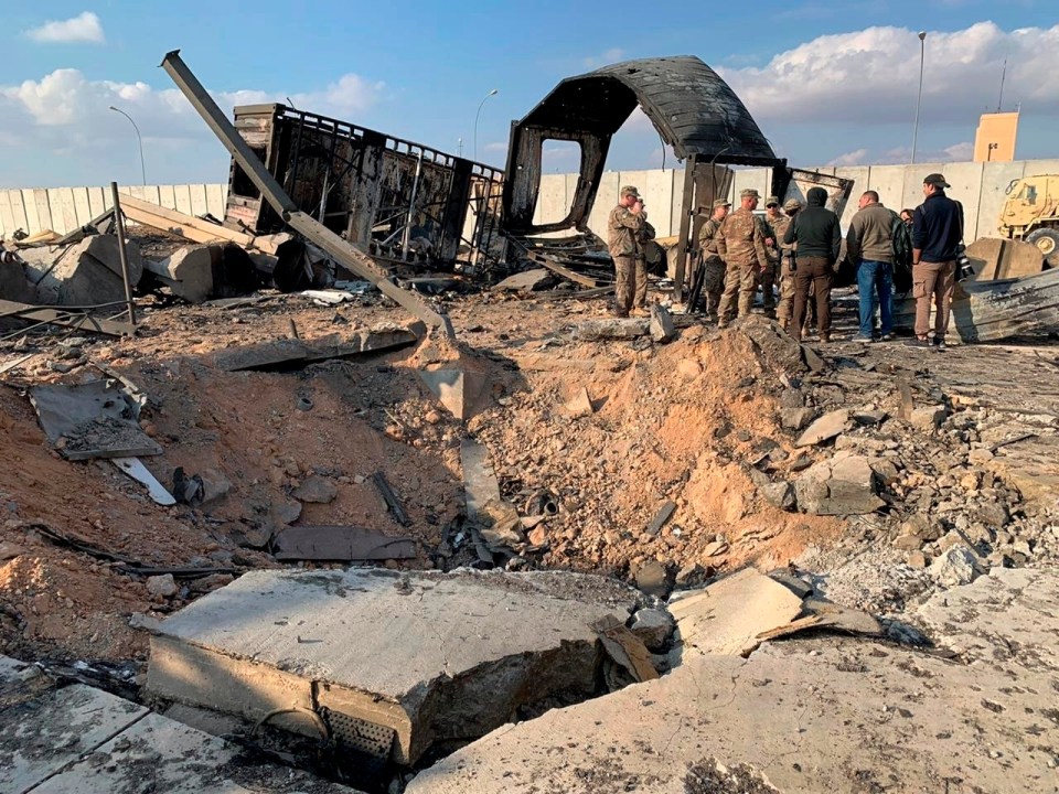 US soldiers and journalists stand by the edge of a huge crater at the Ain al-Asad air base today