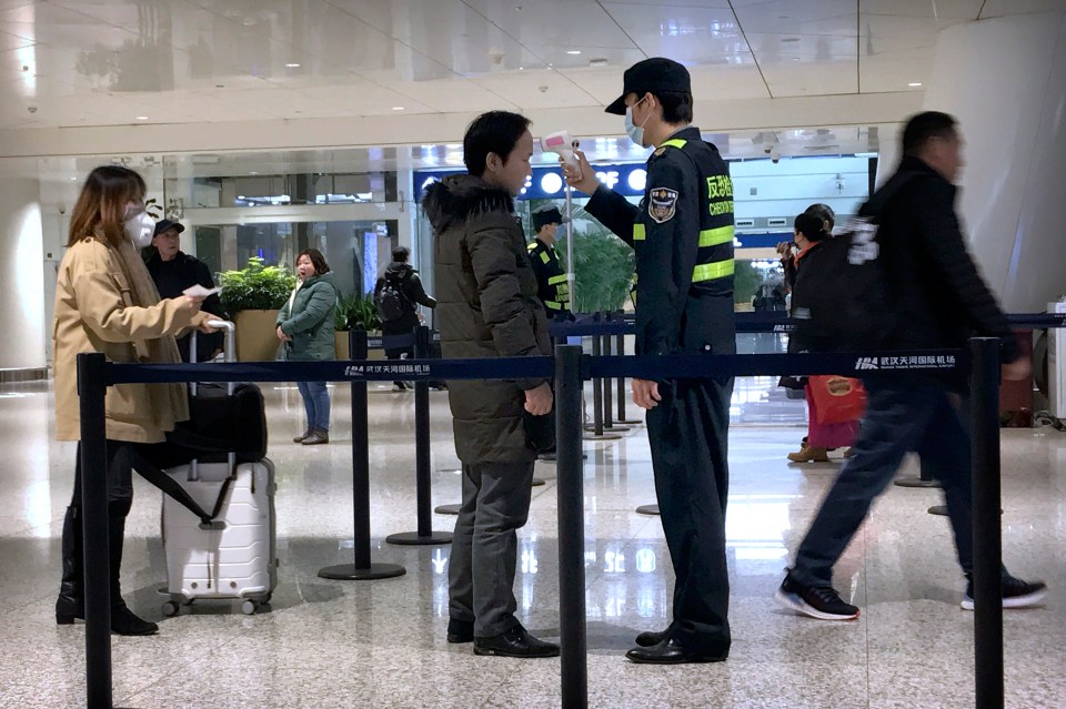 An official uses an infrared thermometer on a traveller at an airport in Wuhan