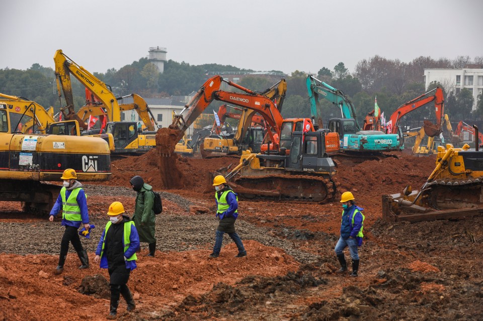 Workers stand amid heavy equipment at a construction site for a field hospital in Wuhan