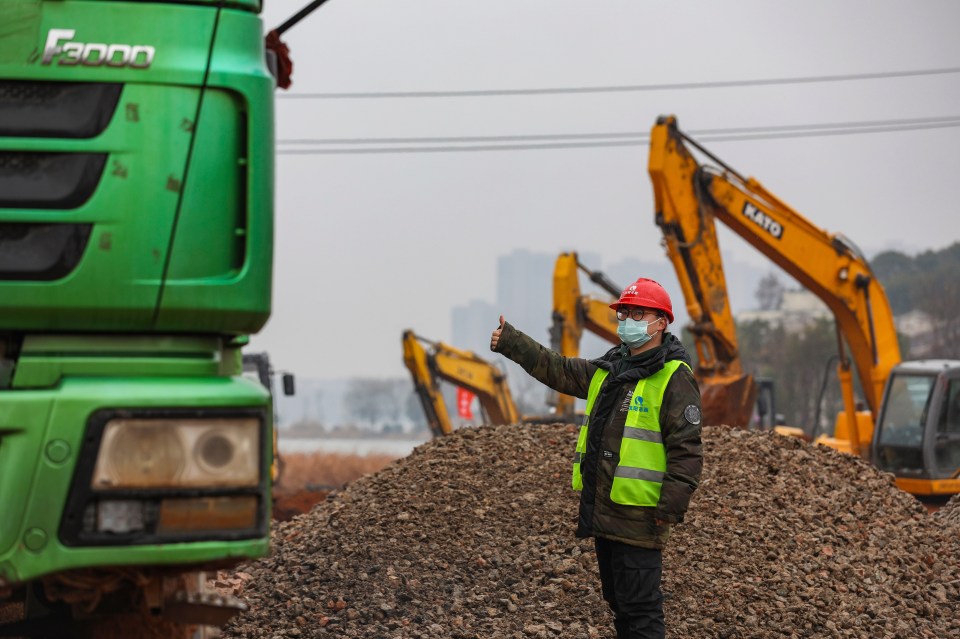 A worker gestures to a truck driver at a construction site for a field hospital in Wuhan