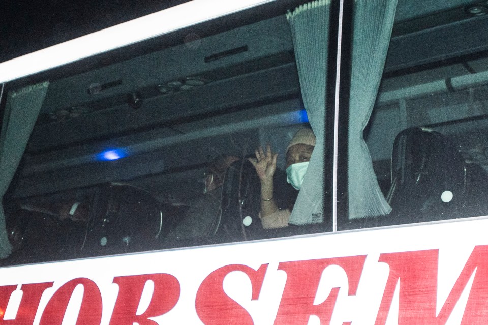  An evacuee wearing a surgical mask waves from one of the buses