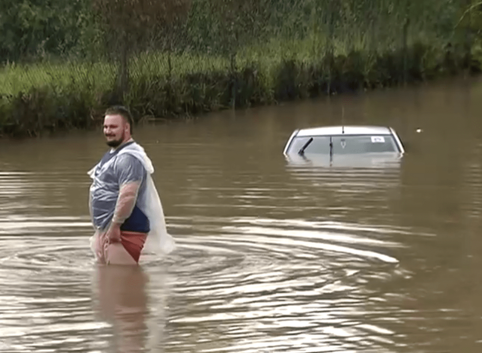  A man stands nearly waist-deep in flood water near a submerged car