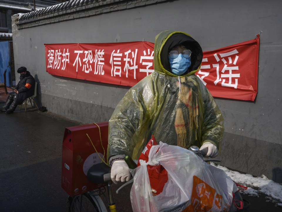 A Chinese woman wears a protective mask, plastic jacket and rubber gloves as she walks home