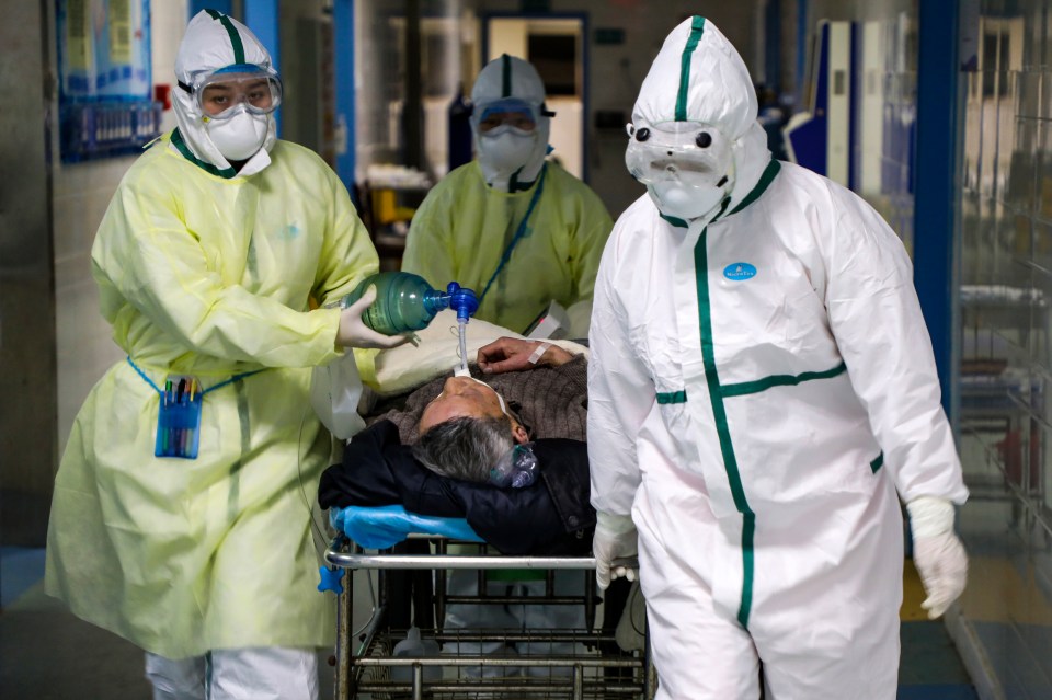 A patient is wheeled out of hospital surrounded by medics in protective suits