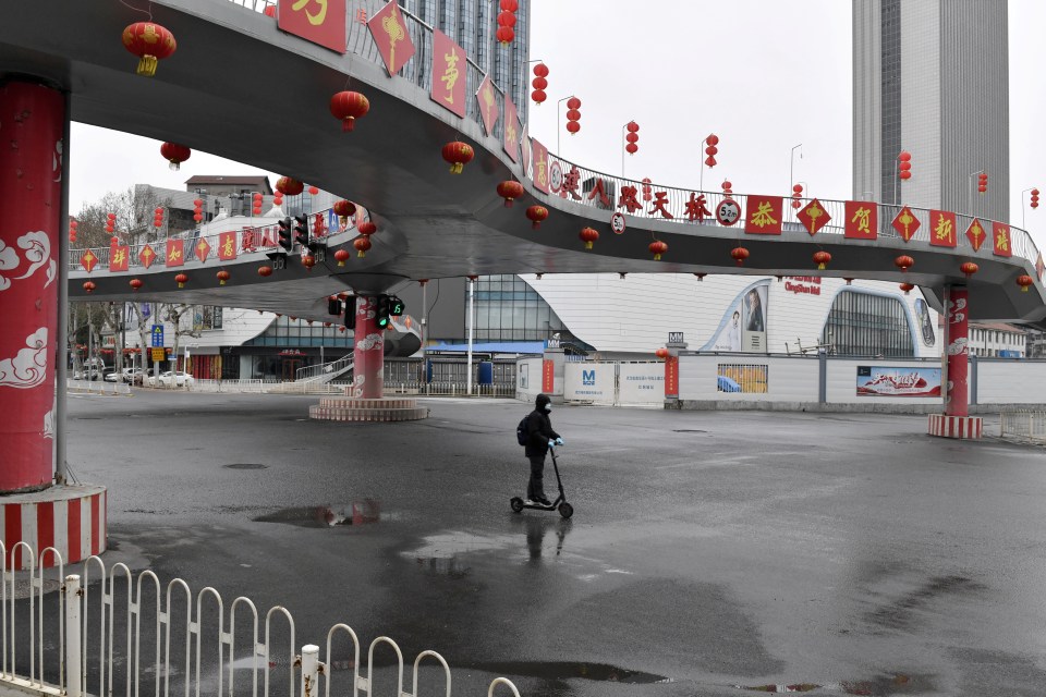 A man on a scooter rides through empty streets in Wuhan